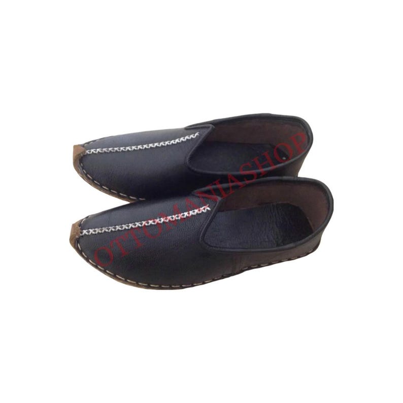 May include: A pair of black leather slip-on shoes with a decorative stitch detail around the toe and heel.