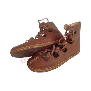 May include: A pair of brown leather sandals with laces that tie up the leg. The sandals have a cut-out design and are made of a soft, supple leather.