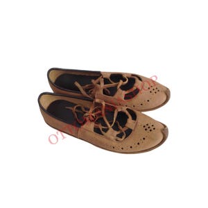 May include: A pair of brown leather shoes with laces and cutouts. The shoes have a pointed toe and a flat sole.