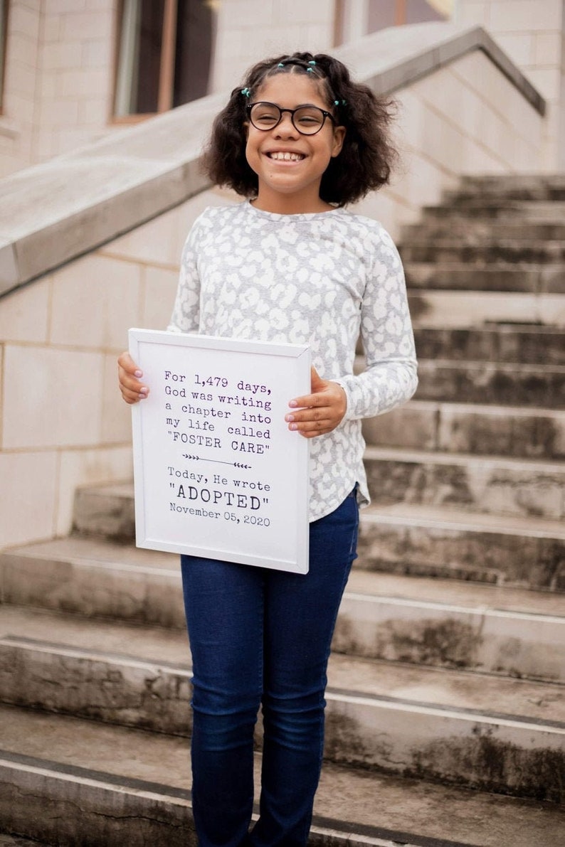 May include: A young person holding a white framed sign with the text "For 1,479 days, God was writing a chapter into my life called "FOSTER CARE" Today, He wrote "ADOPTED" November 05, 2020".