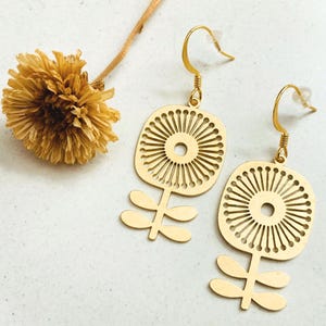 May include: A pair of gold-tone earrings featuring a geometric flower design with a circular center. The earrings have a simple hook closure.