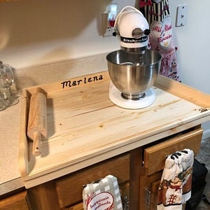 May include: A wooden countertop with a built-in cutting board and a rolling pin. The countertop is labeled "Marlena" and has a white stand mixer on top.