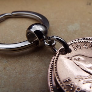 Puede incluir: Primer plano de un llavero con un anillo plateado y un colgante hecho de monedas antiguas. Las monedas tienen un color cobre y presentan un dise&ntilde;o de p&aacute;jaro y el a&ntilde;o 1946. El llavero es probablemente un art&iacute;culo de colecci&oacute;n.