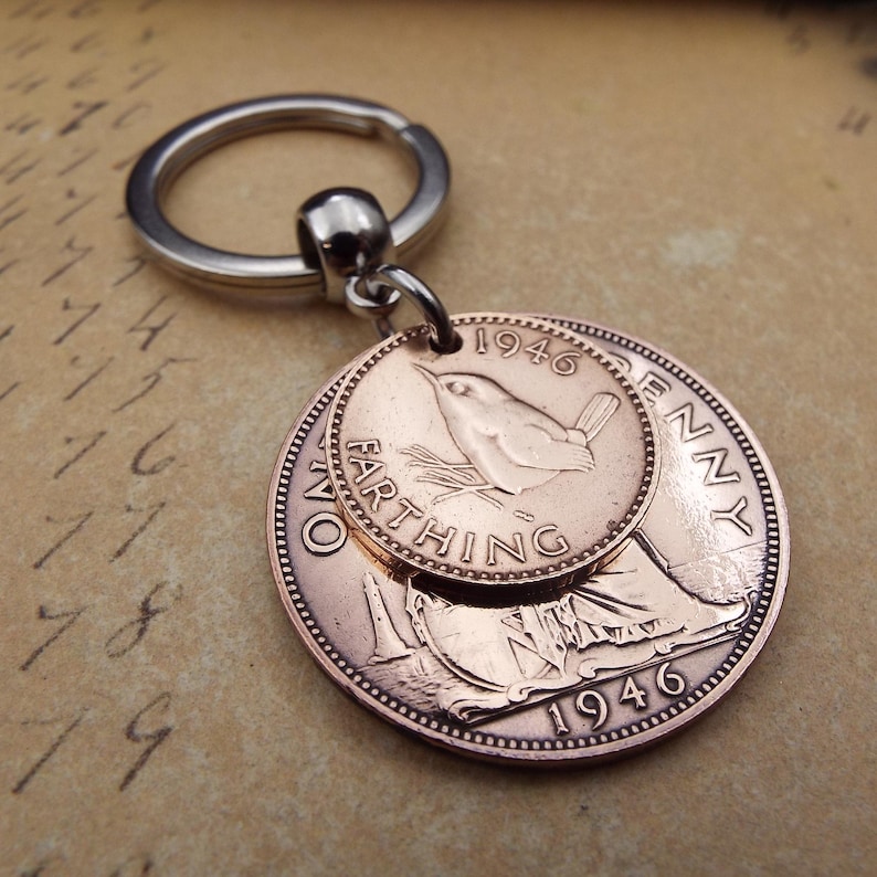 Puede incluir: Un llavero de color cobre con dos monedas antiguas. La moneda m&aacute;s grande muestra una figura sentada y el a&ntilde;o 1946. La moneda m&aacute;s peque&ntilde;a, tambi&eacute;n de 1946, presenta un p&aacute;jaro. El llavero tiene un anillo plateado.