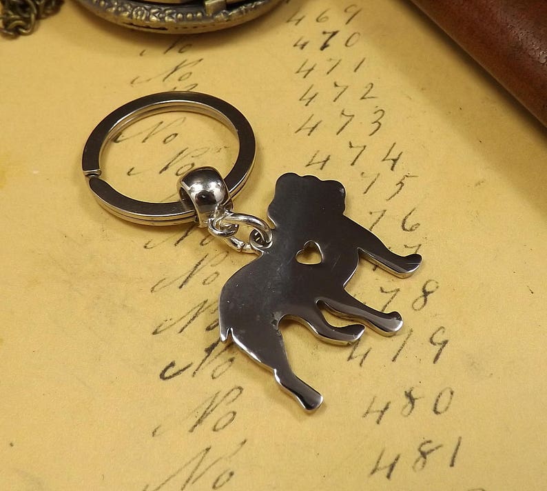 May include: Silver-toned keychain featuring a detailed silhouette of a dog with a heart cutout. The keychain has a silver-toned ring.