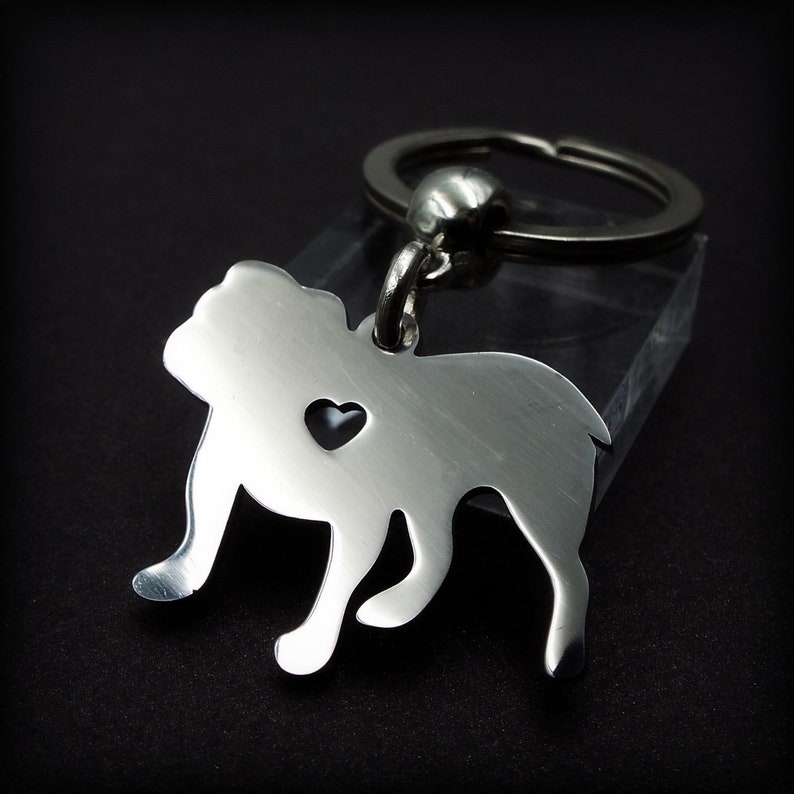 May include: Silver bulldog keychain with a heart cut out. The keychain is attached to a silver key ring.