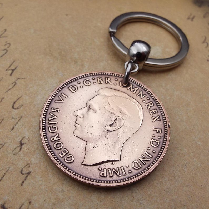 Puede incluir: Un llavero con moneda de color cobre que presenta el perfil de un hombre y el texto "GEORGIVS VI D:G:BR: OMN:REX F:D:IND:IMP." La moneda est&aacute; unida a un llavero plateado.