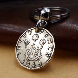 May include: Silver key chain with a 1944 British Three Pence coin charm. The coin features a design of three stylised flowers with stems.