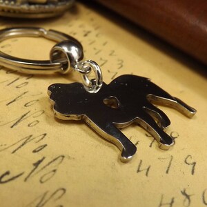 May include: A silver metal keychain featuring a silhouette of a dog. The keychain has a silver metal ring.