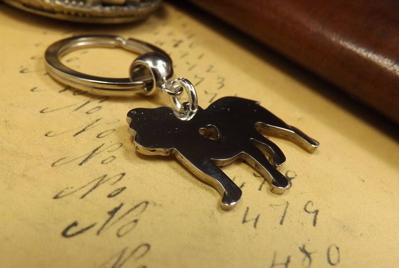 May include: A silver metal keychain featuring a silhouette of a dog. The keychain has a silver metal ring.