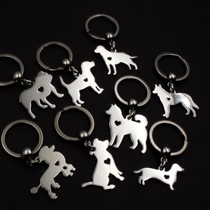 May include: A set of eight silver keychains featuring different dog breeds, each with a small heart cutout. The keychains are attached to silver key rings.