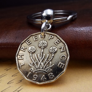 May include: Silver key chain with a 1948 three pence coin charm featuring a floral design. The coin is silver with a gold tone.