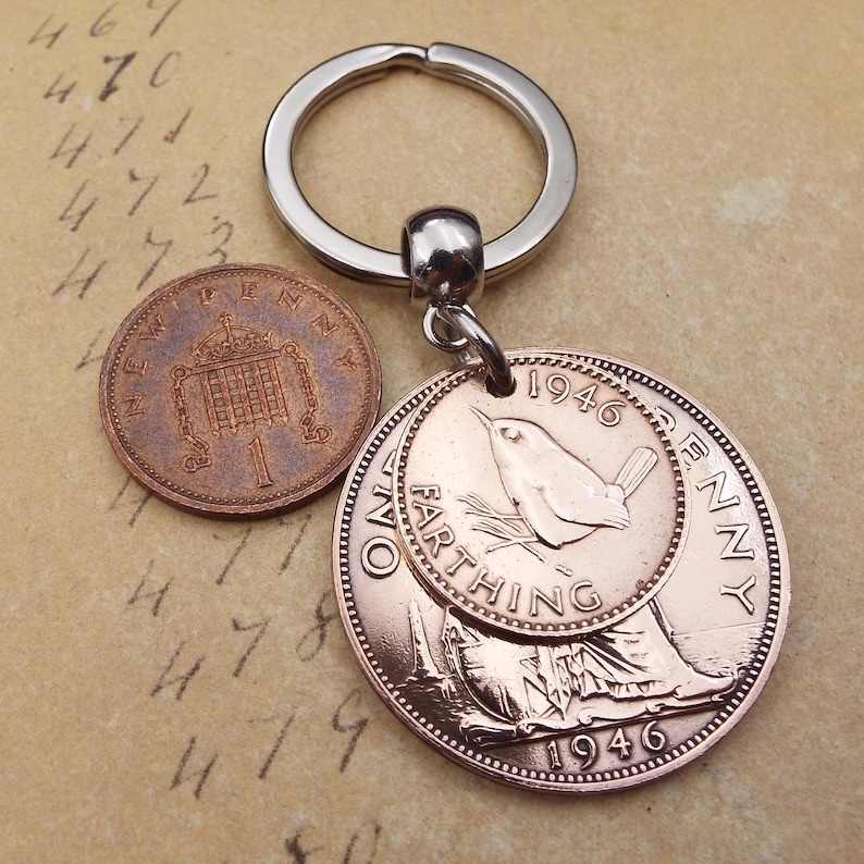 Pu&ograve; includere: Un portachiavi color rame con due monete vintage e un anello color argento. Una moneta &egrave; un penny, e l'altra &egrave; una moneta da farthing del 1946, con un disegno di uccello. Lo sfondo &egrave; una superficie beige con numeri scritti a mano.