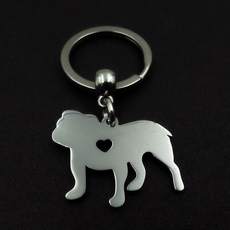 May include: Silver bulldog keychain with a heart cut out. The keychain is attached to a silver key ring.