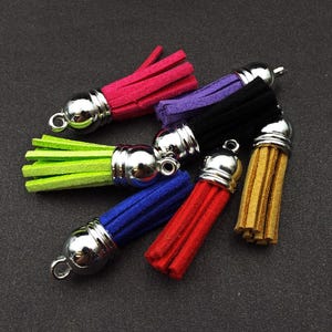 May include: Assortment of six colourful suede tassels with silver metal caps. The tassels are in the colours green, red, blue, black, purple, and brown.