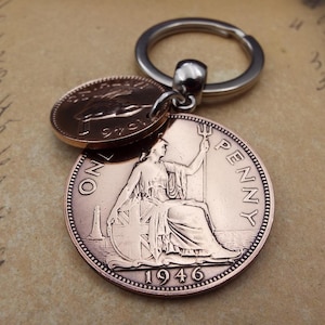 Puede incluir: Un llavero de color cobre con dos monedas brit&aacute;nicas antiguas. La moneda m&aacute;s grande, fechada en 1946, muestra a Britannia sentada y las palabras "ONE PENNY". La moneda m&aacute;s peque&ntilde;a tambi&eacute;n es de color cobre y tiene un dise&ntilde;o similar. El llavero tiene un anillo plateado.