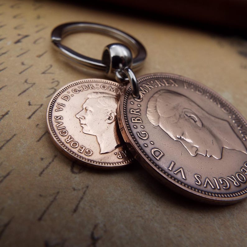 Puede incluir: Un llavero plateado con dos monedas de color cobre. Las monedas muestran perfiles y texto alrededor de los bordes. El llavero est&aacute; unido a las monedas por un peque&ntilde;o lazo plateado.