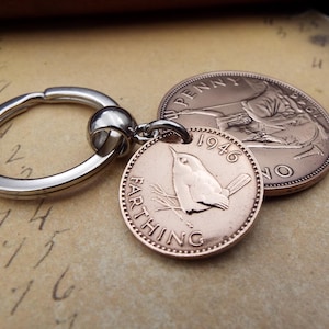 Pu&ograve; includere: Portachiavi con una moneta Farthing del 1946, con un disegno di uccello, attaccato a un portachiavi argentato. Una moneta Penny &egrave; visibile sullo sfondo. Le monete sono di colore rame.