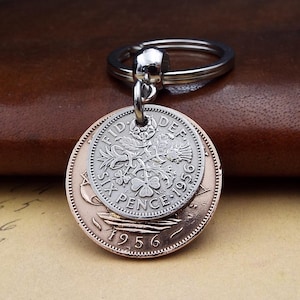 May include: A silver keyring with a vintage coin pendant. The pendant features two coins, one silver and one copper-coloured, with detailed designs and the year 1956 visible. The keyring is attached to a silver ring.