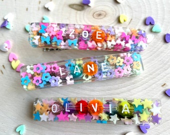 May include: Three clear plastic hair clips with colorful beads and letters spelling out the names "Zoe", "Lane", and "Olivia".