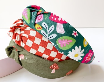 May include: Three fabric headbands with different patterns. The top headband is green with a floral and mushroom design. The middle headband is red and white checkered. The bottom headband is olive green with a mushroom design.