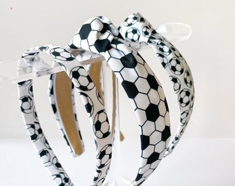 May include: Three black and white soccer ball patterned headbands. The headbands are tied in a knot at the top.