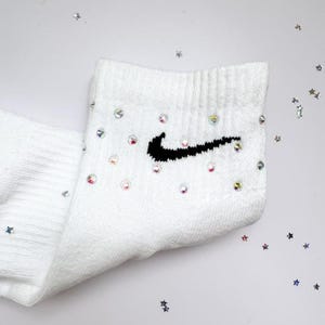 May include: White ankle socks with a black Nike swoosh and rhinestones.