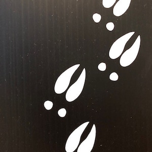 May include: A black background with a series of white deer hoof prints. The prints are arranged in a diagonal line from the top right corner to the bottom left corner of the image.