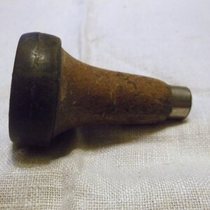 May include: A wooden and metal tool with a black rubber handle. The tool is used for making holes in leather.