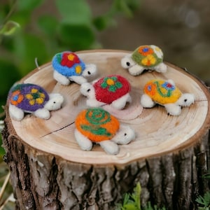 Könnte beinhalten: Sechs Filzturtel-Figuren mit bunten Blumenmustern auf einem Baumstumpf. Die Schildkröten sind in verschiedenen Farben, darunter Rot, Blau, Grün, Gelb und Lila.