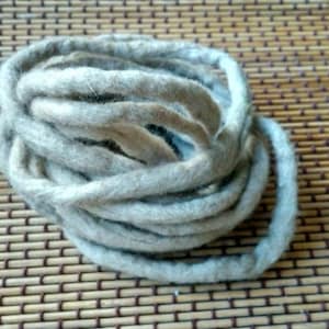 May include: A close-up of a bundle of light grey and beige yarn. The yarn is soft and fluffy, and it is perfect for crocheting or knitting.
