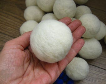 May include: A hand holding a white wool dryer ball. The ball is surrounded by other white wool dryer balls.