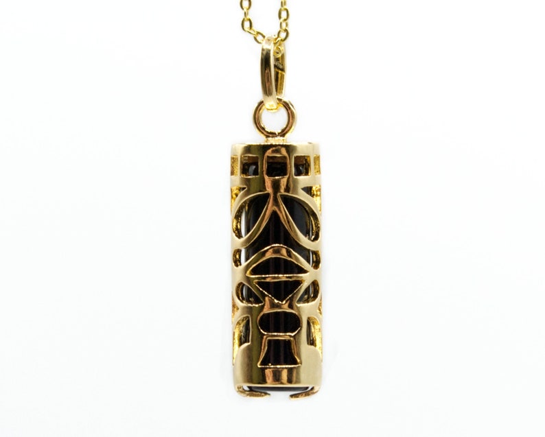 May include: A gold-colored pendant necklace with a cylindrical, openwork design. The pendant has a dark interior and hangs from a delicate gold chain. The intricate pattern of the pendant is visible against a white background.