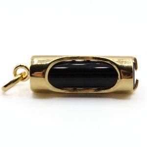 May include: A gold-colored pendant with a black, cylindrical stone set in the center. The pendant has a rounded rectangular shape with an oval opening on each side, and a small loop for attaching to a chain.