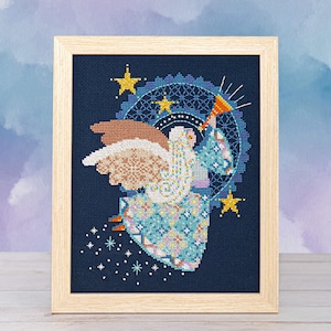 Könnte beinhalten: Kreuzstich-Kunst eines Engels mit gemusterten Flügeln und einem blau-weiß gemusterten Kleid, das eine Trompete hält. Das Kunstwerk ist in einem hellen Holzrahmen gerahmt, vor einem dunkelblauen Hintergrund mit Sternen und einem dekorativen Kreis.