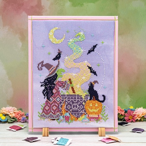 May include: A cross-stitch pattern depicting two witches stirring a cauldron beneath a crescent moon and stars. The witches are wearing colourful robes and hats. A black cat sits on a pumpkin beside the cauldron.