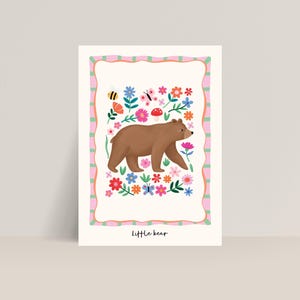 May include: A whimsical illustration of a brown bear walking through a field of colorful flowers, butterflies, and a bee. The artwork is framed with a pink and green border and the words "Little bear" are at the bottom.