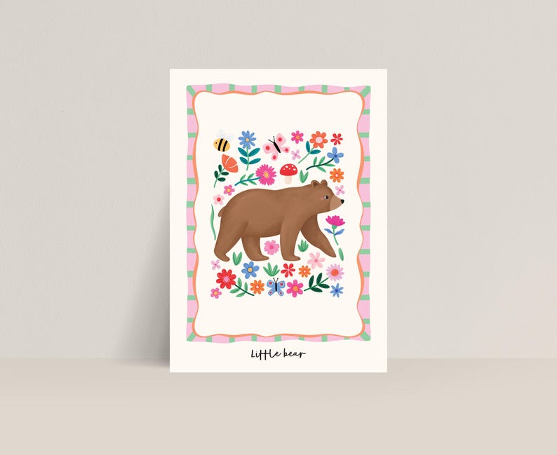 May include: A whimsical illustration of a brown bear walking through a field of colorful flowers, butterflies, and a bee. The artwork is framed with a pink and green border and the words "Little bear" are at the bottom.