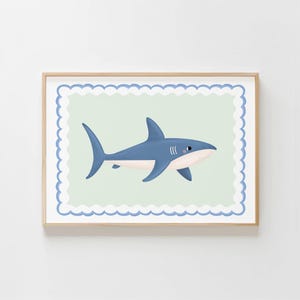 May include: A framed print featuring a blue shark illustration. The shark is depicted in a side profile with a white belly and a light blue body. The background is a light green colour with a scalloped border.