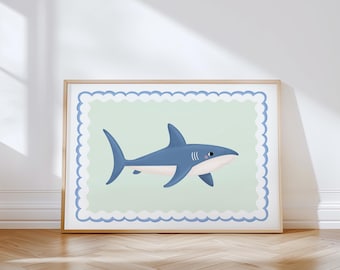 May include: A framed print featuring a cartoon shark illustration. The shark is blue with white accents and is set against a light green background with a blue scalloped border. The frame is a light wood color.