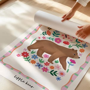 May include: A rolled-up poster featuring a brown bear illustration surrounded by colorful flowers, butterflies, and a mushroom. The poster has a pink and green border and the words "Little bear" at the bottom.