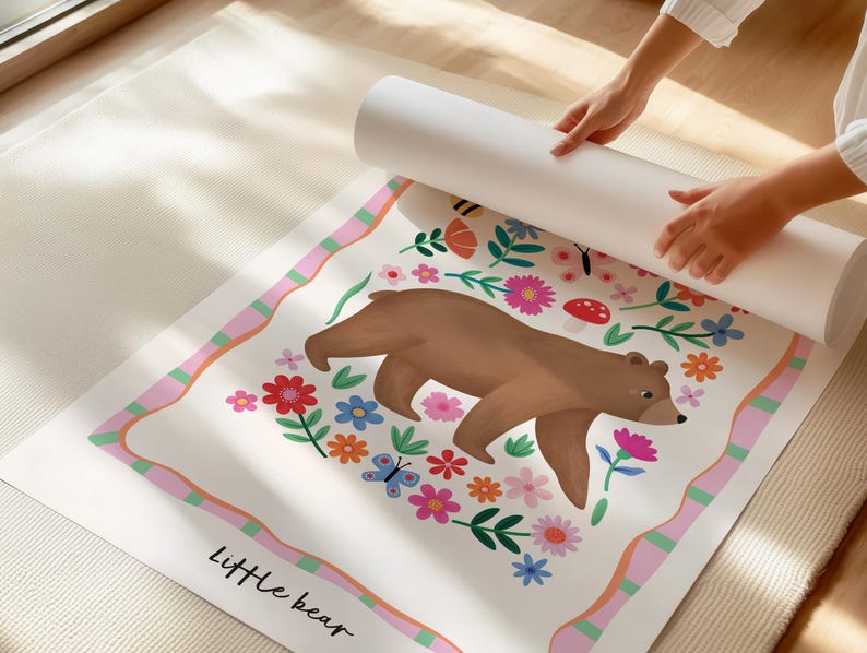 May include: A rolled-up poster featuring a brown bear illustration surrounded by colorful flowers, butterflies, and a mushroom. The poster has a pink and green border and the words "Little bear" at the bottom.
