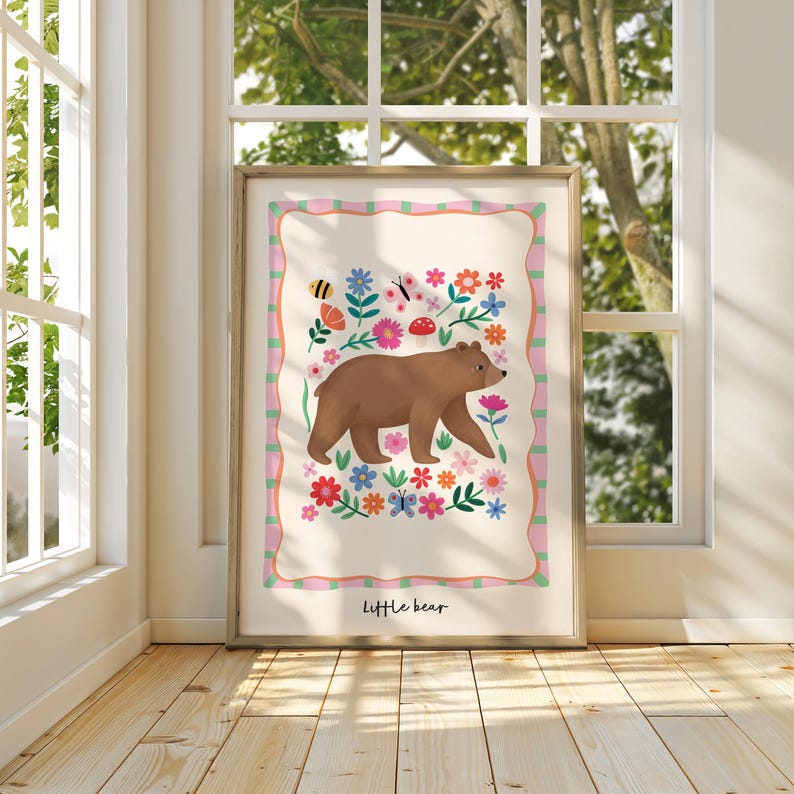 May include: A framed art print featuring a brown bear walking among colorful flowers, butterflies, and a bee. The artwork has a pink and green border and the words "little bear" at the bottom.