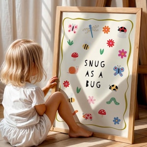Peut inclure: Une affiche encadrée avec un cadre en bois clair. L'impression présente des illustrations colorées d'insectes, de fleurs et d'un escargot, avec le texte "SNUG AS A BUG" en noir. L'impression est sur un fond crème.
