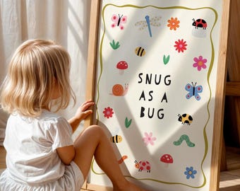May include: A framed art print with a light wood frame. The print features colorful illustrations of bugs, flowers, and a snail, with the text "SNUG AS A BUG" in black. The print is on a cream background.