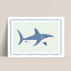 May include: A framed print featuring a cartoon shark. The shark is blue with a white belly and a small pink blush on its cheek. It is set against a light green background within a blue scalloped border.
