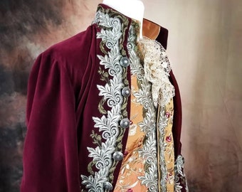 May include: A burgundy velvet jacket with silver and gold embroidery. The jacket has a high collar and long sleeves. The jacket is worn over a gold and white patterned vest.