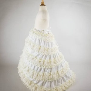 K&ouml;nnte beinhalten: Ein wei&szlig;er Petticoat mit mehreren Schichten gekr&auml;uselter Spitze. Der Petticoat befindet sich auf einem wei&szlig;en Mannequin und hat einen langen, flie&szlig;enden Rock.