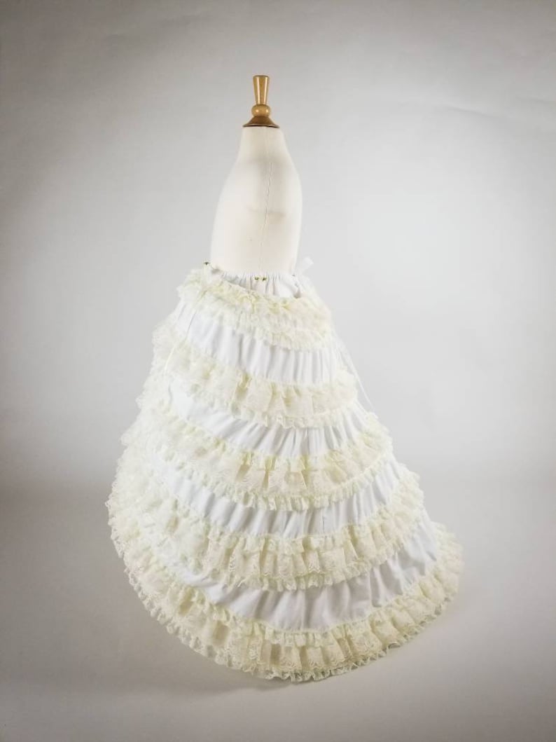 K&ouml;nnte beinhalten: Ein wei&szlig;er Petticoat mit mehreren Schichten gekr&auml;uselter Spitze. Der Petticoat befindet sich auf einem wei&szlig;en Mannequin und hat einen langen, flie&szlig;enden Rock.