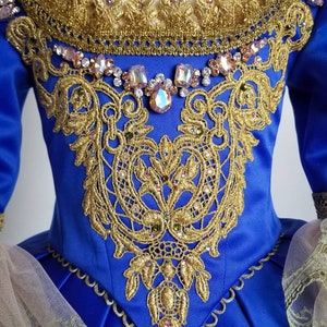 K&ouml;nnte beinhalten: Ein blaues Satin-Kleid mit goldener Spitze und Kristallverzierungen. Das Kleid hat einen herzf&ouml;rmigen Ausschnitt und ein tailliertes Oberteil. Der Rock ist voll und flie&szlig;end.